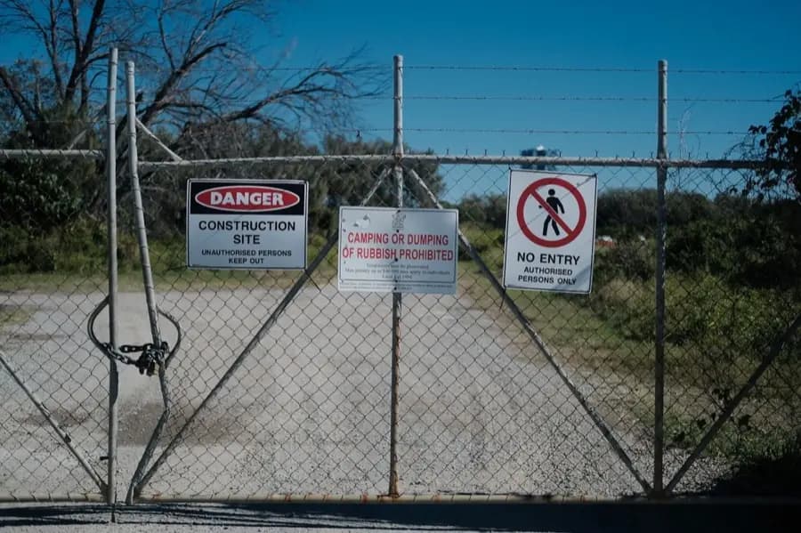 A padlocked construction site gate carrying Danger, No Entry and No Dumping signs